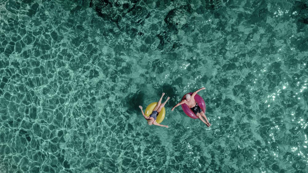 Couple in an inner tube floating over clear water, rerpesenting the value of transparency around retirement planning.